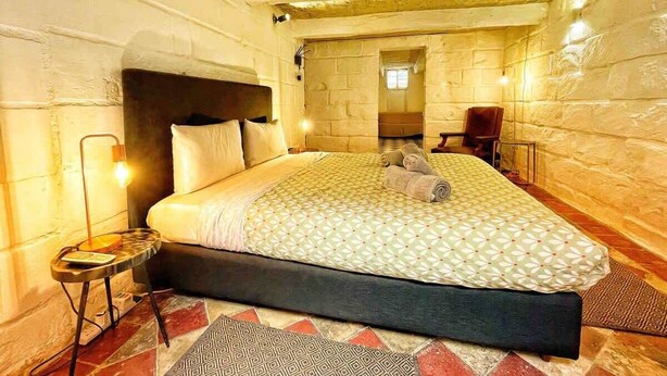 Ein Schlafzimmer mit Bett, Nachttisch, Lampe und Blick auf ein Badezimmer.