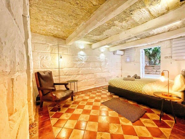 A room with a checkered floor, a bed, a chair, and a lamp.