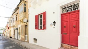 Straßenansicht eines weißen Gebäudes mit roten Fensterläden und -türen, Hausnummer 44, und einem schmiedeeisernen Geländer über der Tür.