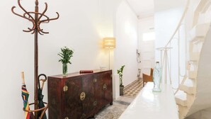 A hallway with a coat rack, a wooden cabinet, a lamp, and a staircase.