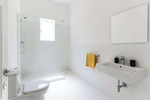 A bathroom with a toilet, shower, sink, and a mirror.