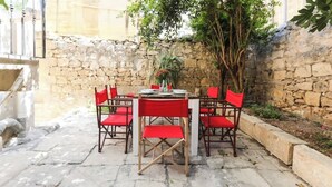 An outdoor patio with a stone wall, a round table with red chairs, and a potted plant.