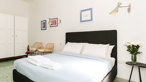A bedroom with a bed, two chairs, a small table, a lamp, and a vase with flowers.
