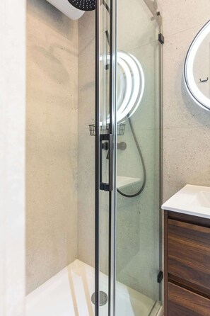 A glass-enclosed shower with a hand showerhead and a wall-mounted mirror.