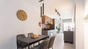 A modern kitchen with a dining area, a clock on the wall, and a visible fire extinguisher. - FL2 Sliema Cozy 1BR Getaway with Balcony (Sliema)