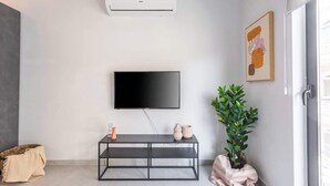 A modern living room with a flat-screen TV mounted on the wall, a black console table with decorative items, a potted plant, and a basket. - FL2 Sliema Cozy 1BR Getaway with Balcony (Sliema)