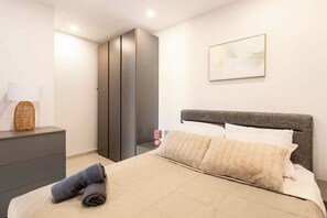 A bedroom with a bed, a wardrobe, a bedside table with a lamp, and a framed picture on the wall.