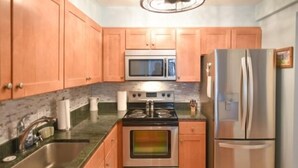 A kitchen with wooden cabinets, a stainless steel refrigerator, a microwave, a stove, and a sink. - Spacious 2 BR 2 Bath Ocean Front building overlooking Pool (Ocean City)