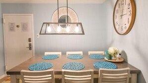 A dining area with a wooden table, six chairs, a wall clock, and a pendant light fixture. - Spacious 2 BR 2 Bath Ocean Front building overlooking Pool (Ocean City)