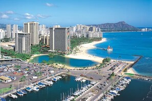 Een kuststadsgezicht met hoge gebouwen, een jachthaven vol boten en een strand met uitzicht op de oceaan en een berg in de verte.