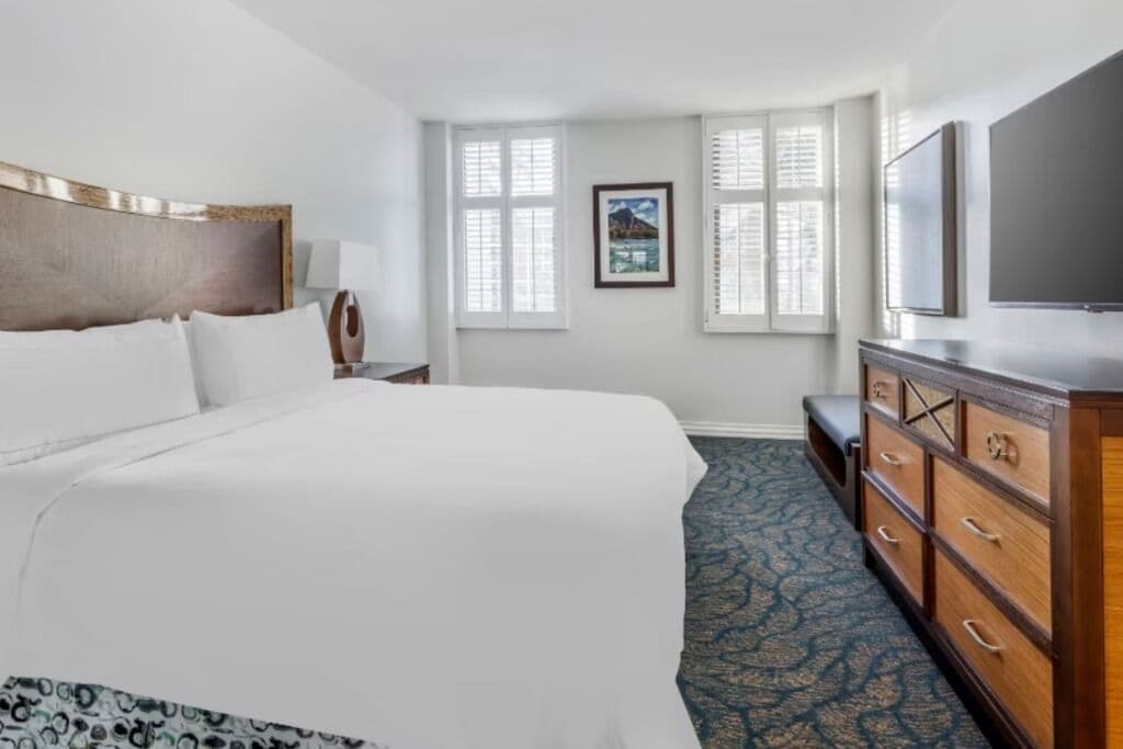 Une chambre d’hôtel avec un lit, une commode, une télévision et une fenêtre avec des stores.