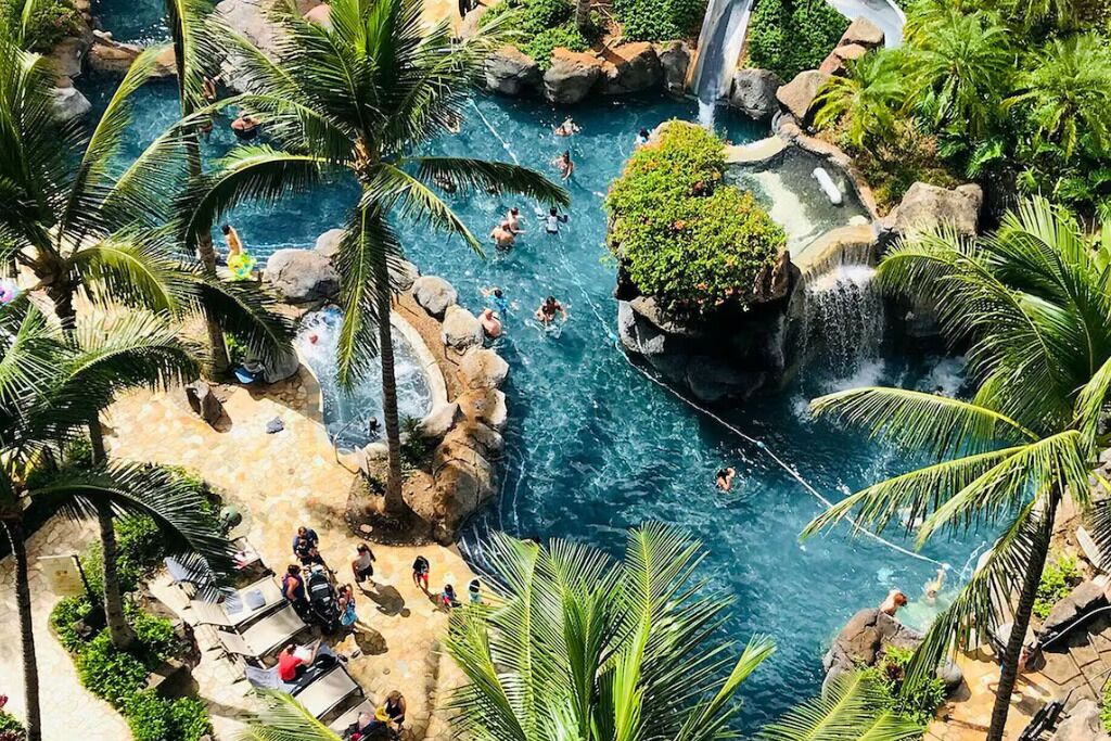 Um resort tropical com várias piscinas, palmeiras e uma cascata.