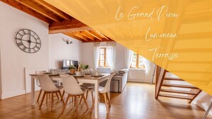 A modern dining area with a wooden table and chairs, a clock on the wall, and a view of the living area. - Le Grand Pirou Lumineux Halte Auvergne (Thiers)
