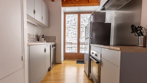 A modern kitchen with stainless steel appliances, wooden flooring, and a view of a snowy outdoor area. - Le Grand Pirou Lumineux Halte Auvergne (Thiers)