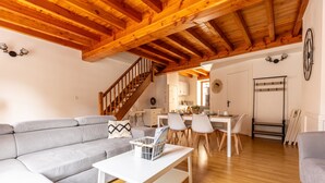A spacious living area with a wooden ceiling, a grey sofa, a white coffee table, and a dining area with chairs and a table. - Le Grand Pirou Lumineux Halte Auvergne (Thiers)