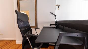 A modern office space with a black office chair, a desk with a laptop, and a large mirror on the wall.