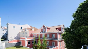 A courtyard with buildings featuring red and white facades, a clear blue sky, and a large tree. - Designer Flats in Lapa by LovelyStay (Lisbon)