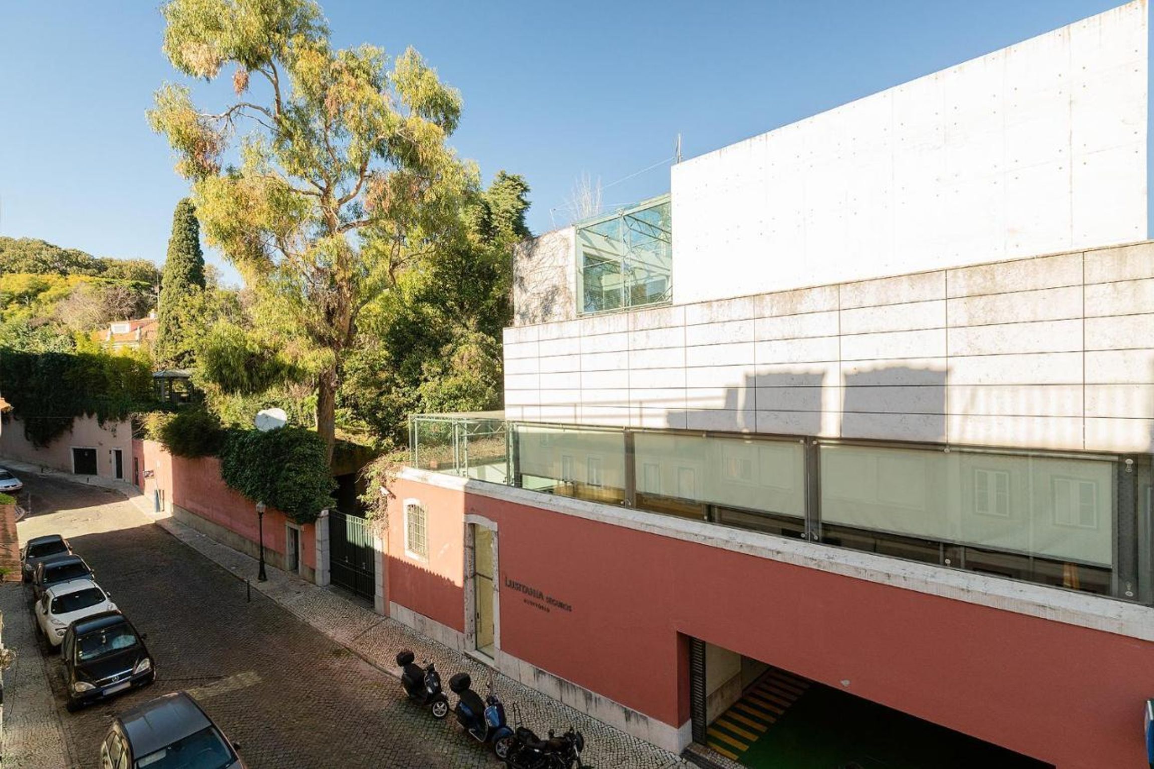 Un edificio con fachada roja, un cerramiento de vidrio y coches y scooters estacionados.