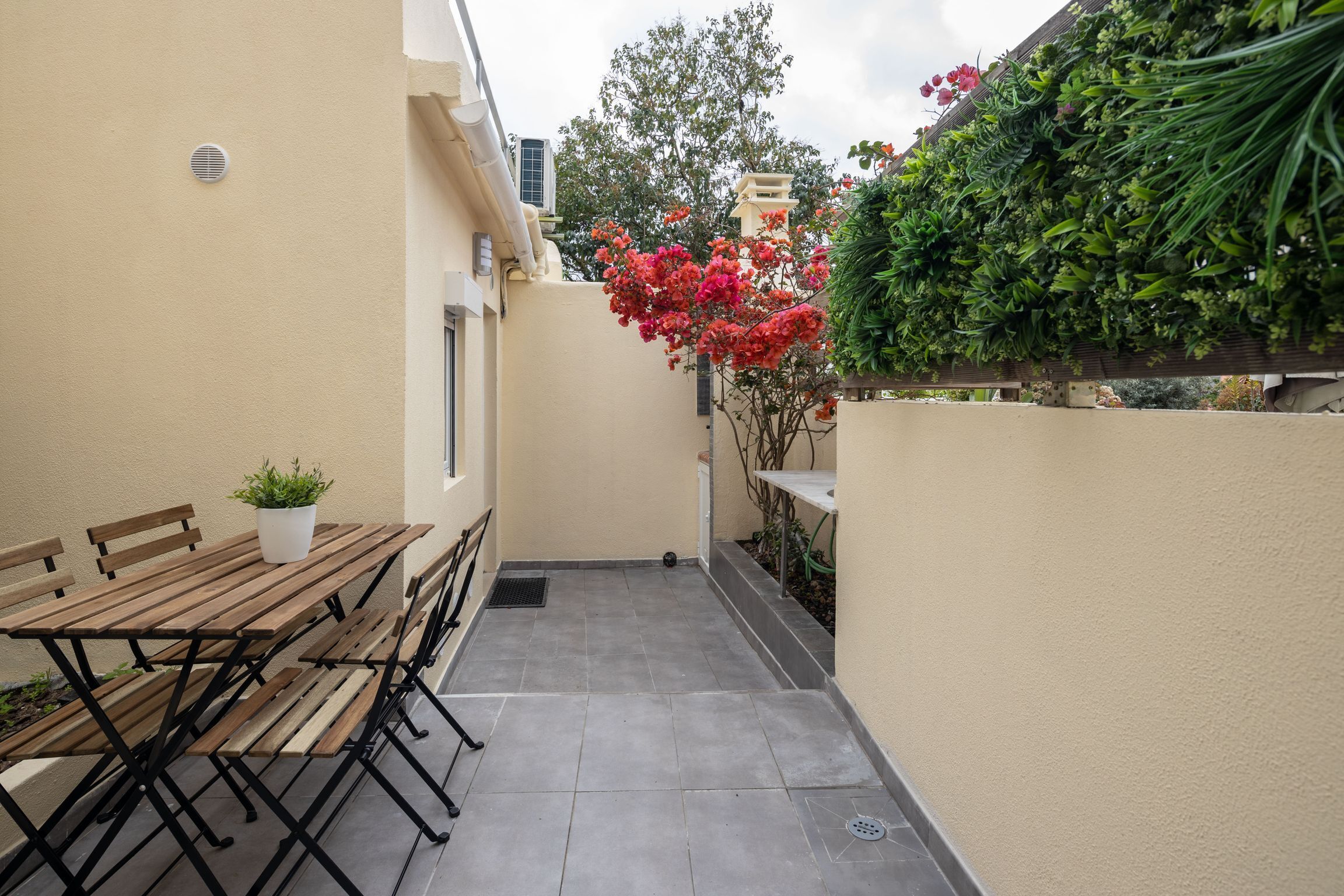 A patio with a wooden table and benches, a small potted plant, and a wall-mounted air conditioning unit.