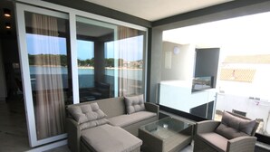 A balcony with wicker furniture, a glass table, and a view of the sea.
