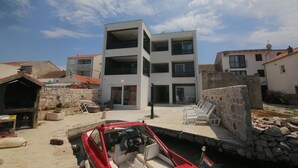A modern multi-story building with a pool area and a red boat docked nearby.