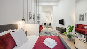 Une chambre d’hôtel moderne, équipée d’un lit, d’un canapé rouge, d’une télévision et d’un coin repas avec une table et des chaises.