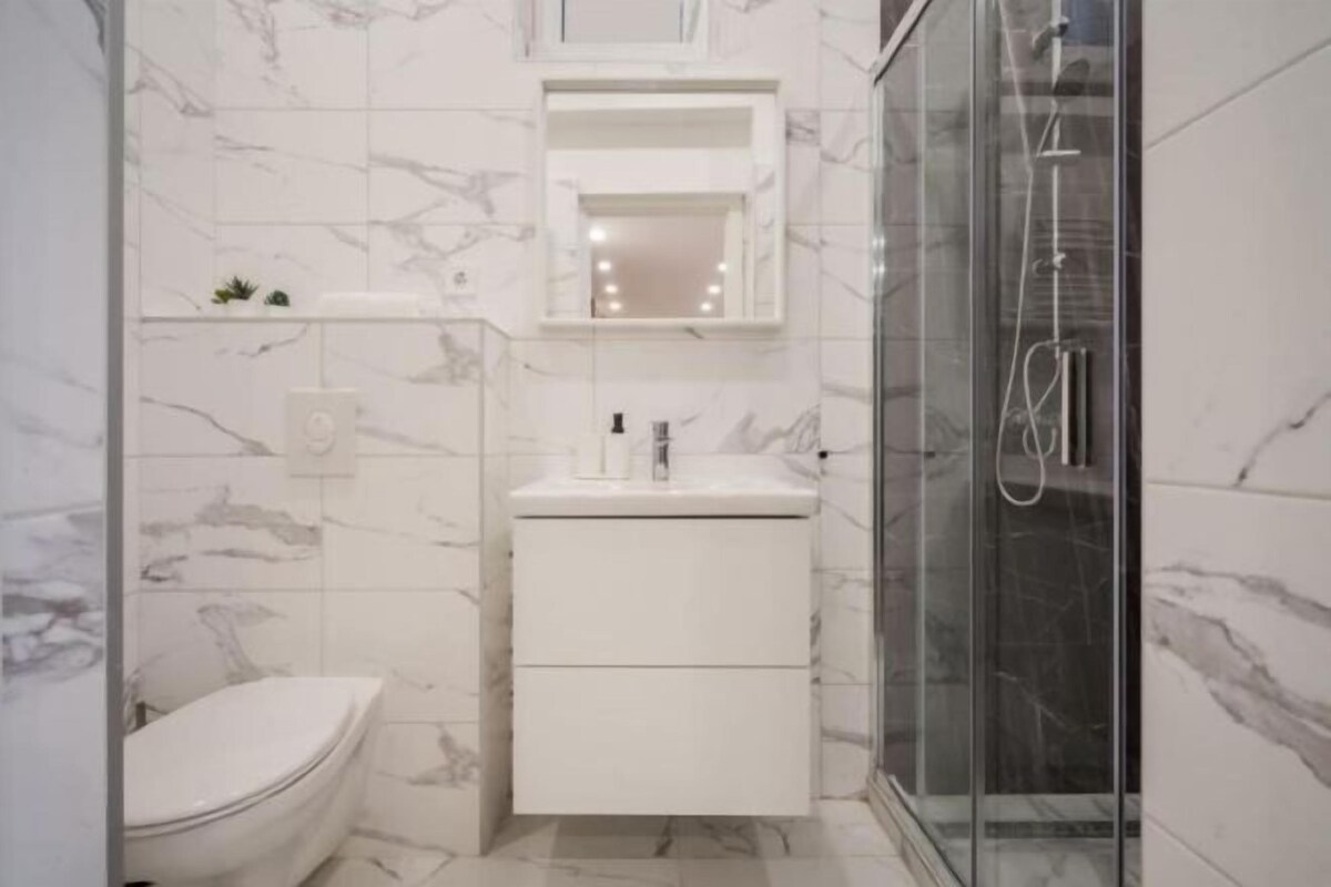 Une salle de bain comprenant des toilettes, un lavabo avec un miroir au-dessus, et une douche séparée par une paroi en verre.