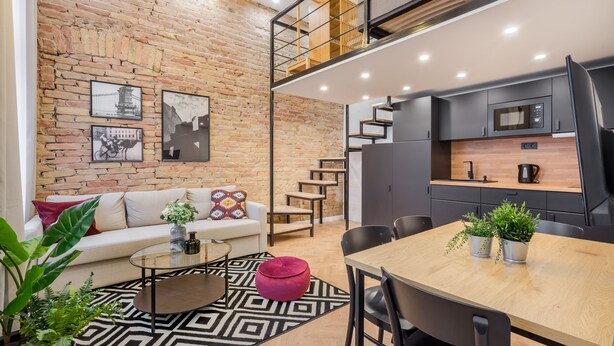 Un espace de vie moderne comprenant un mur en briques, un espace en mezzanine, une table à manger avec des chaises et une cuisine équipée d’un four à micro-ondes.