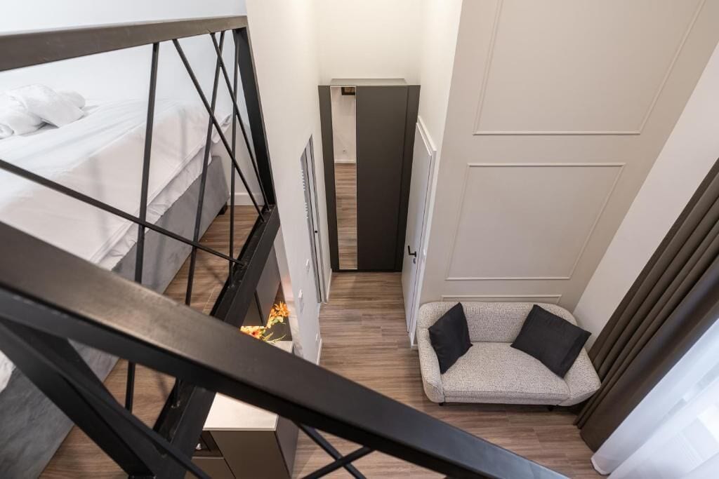 Un couloir étroit, avec un lit sur la gauche, un canapé avec des coussins sur la droite et une porte au fond.