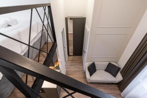 Un pasillo estrecho con una cama a la izquierda, un sofá con cojines a la derecha y una puerta al final.