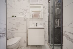 Un baño moderno con inodoro, lavamanos con espejo arriba y cabina de ducha con paredes de vidrio.