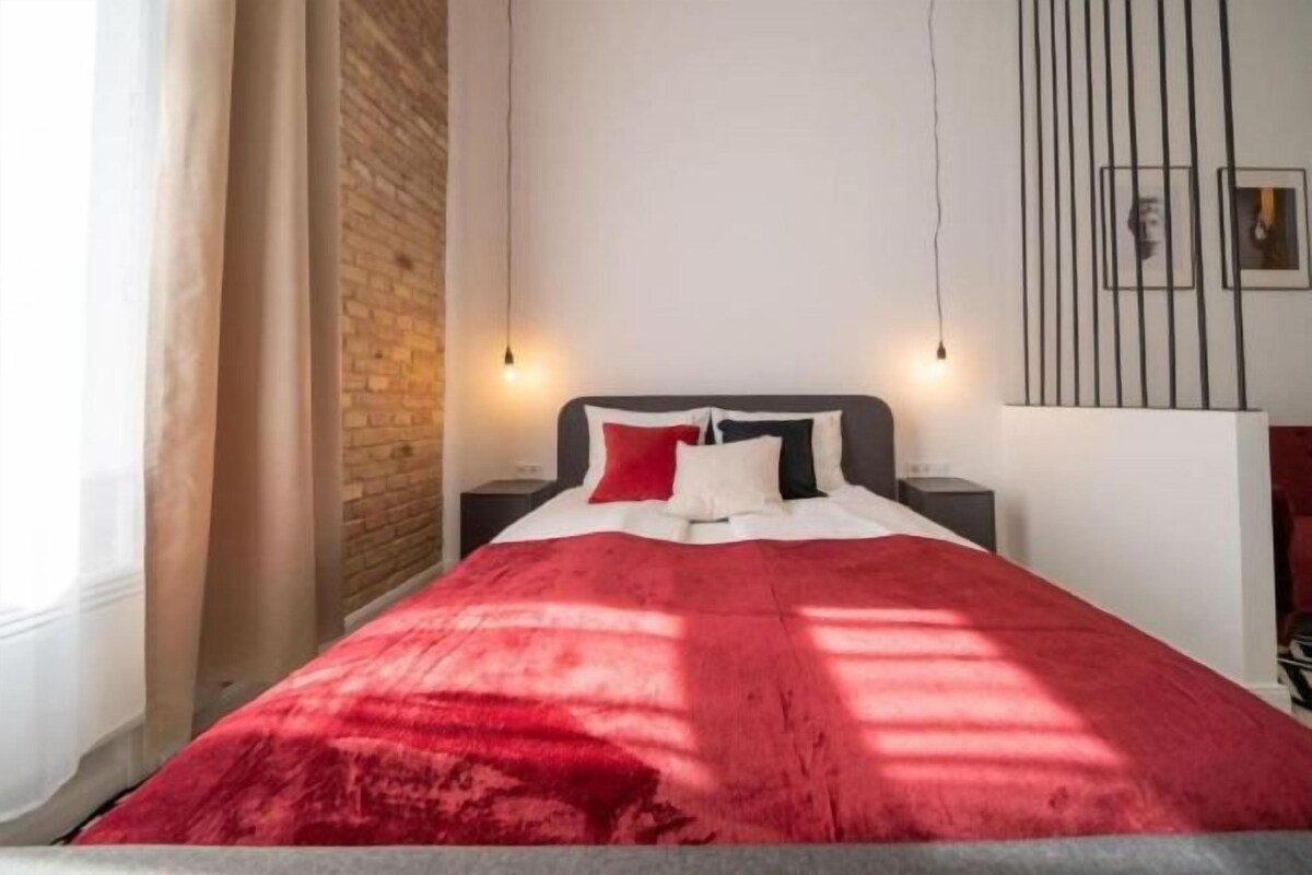 Une chambre à coucher moderne avec une couvre-lit rouge, un mur en briques et une décoration minimaliste.