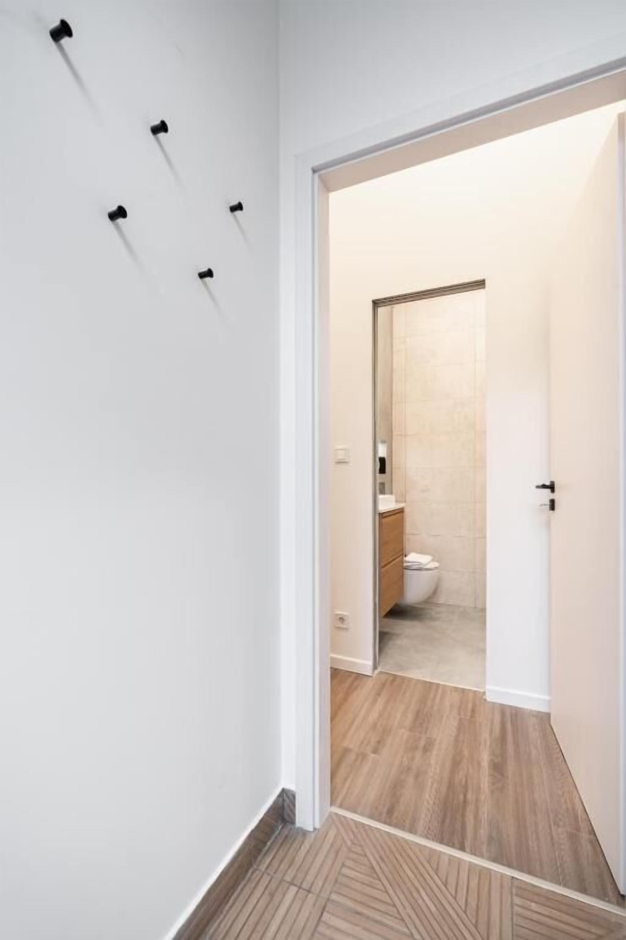 Um corredor com piso de madeira que leva a um banheiro com vaso sanitário e pia.
