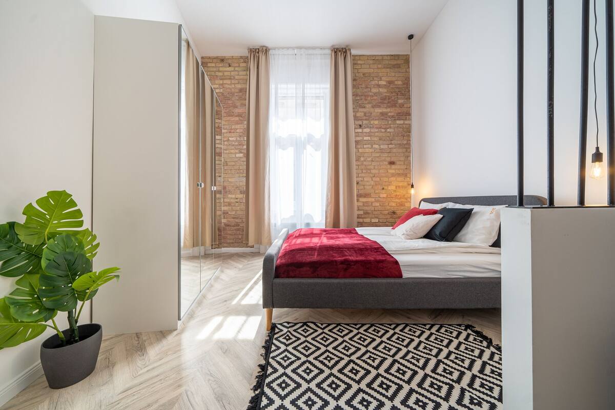 Ein modernes Schlafzimmer mit einem Bett, einer Topfpflanze und einem gemusterten Teppich.