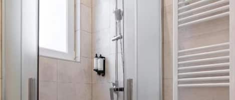 Eine Duschkabine mit Glaswänden, ein weiß gefliester Boden und ein Handtuchhalter an der Wand.