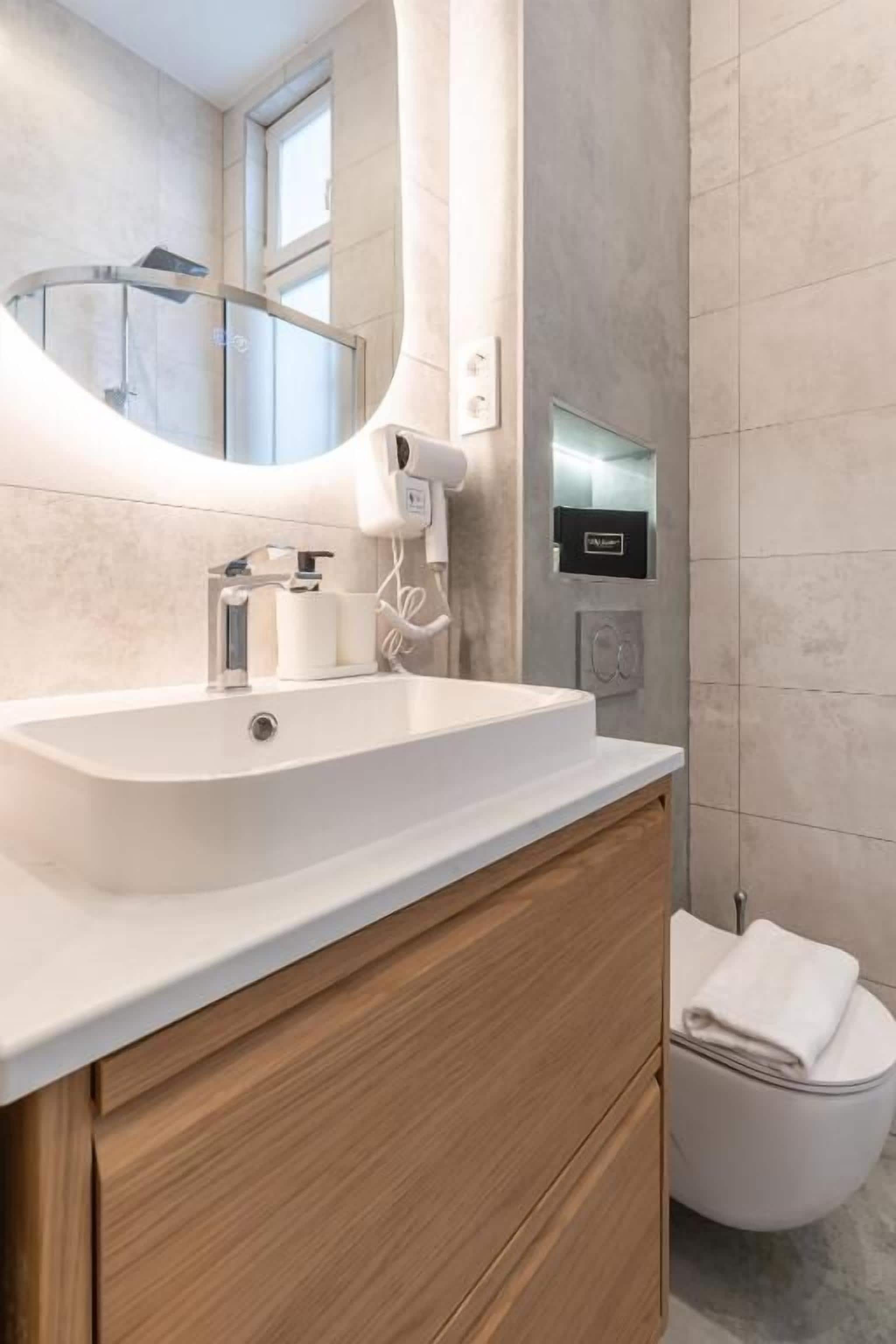 Une salle de bain moderne avec un lavabo blanc, un meuble-lavabo en bois, un porte-serviettes et des toilettes.