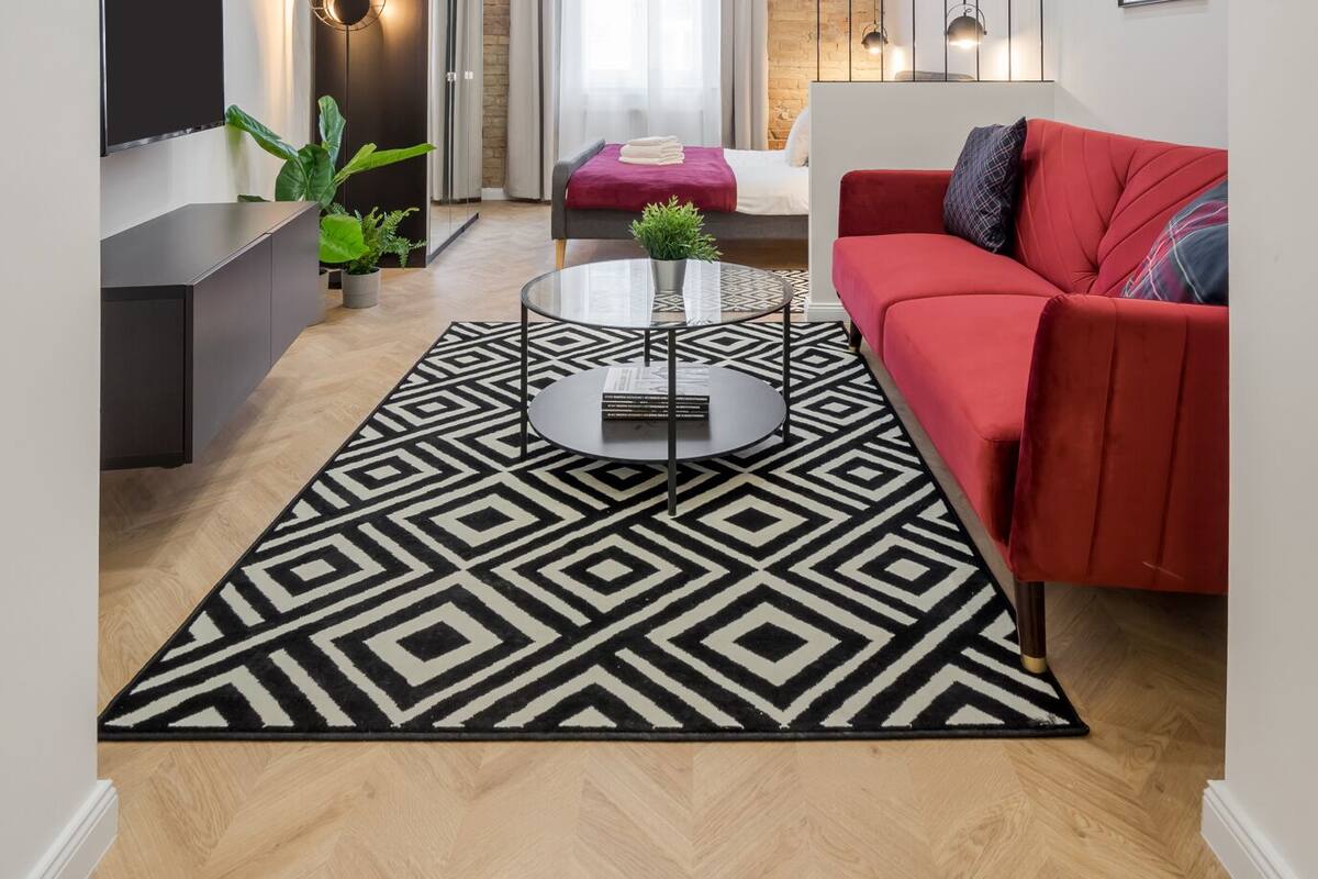 Ein modernes Wohnzimmer mit einem roten Sofa, einem schwarz-weißen Teppich, einem an der Wand montierten Fernseher und einer Ziegelwand.