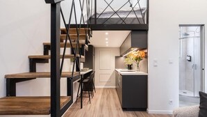 Une cuisine moderne dotée d’un îlot central, d’un coin repas avec une table et des chaises, et d’un escalier avec des marches en bois et des rampes en métal noir.