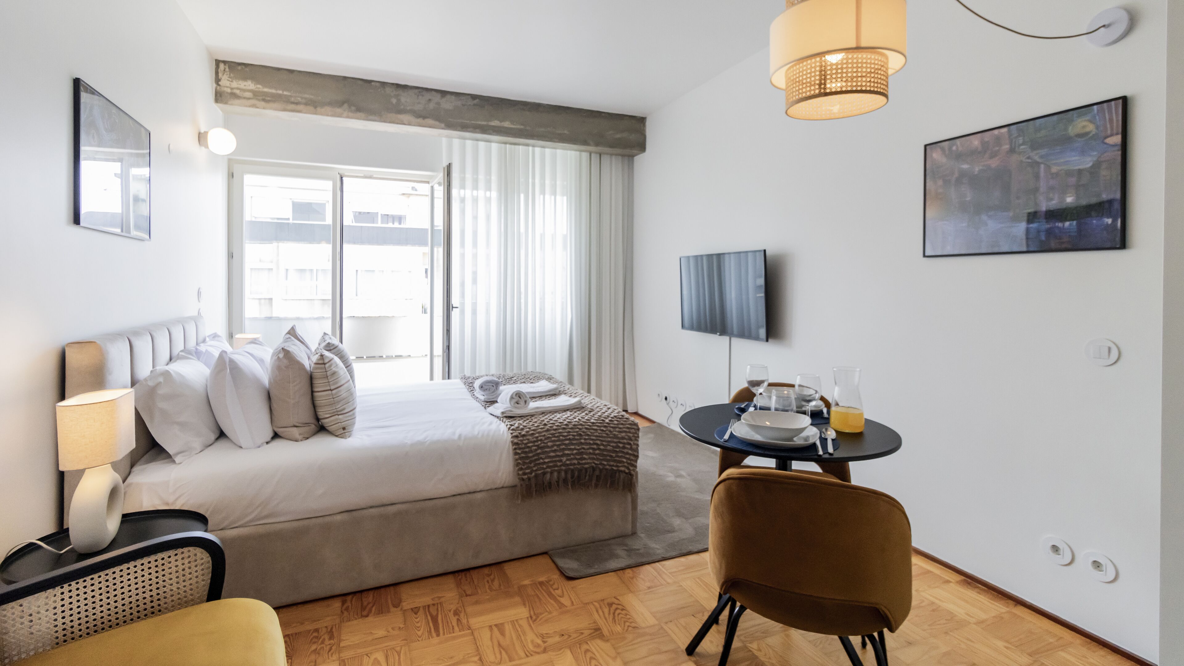 A modern hotel room with a large bed, a desk with a chair, a television, and a window with curtains.