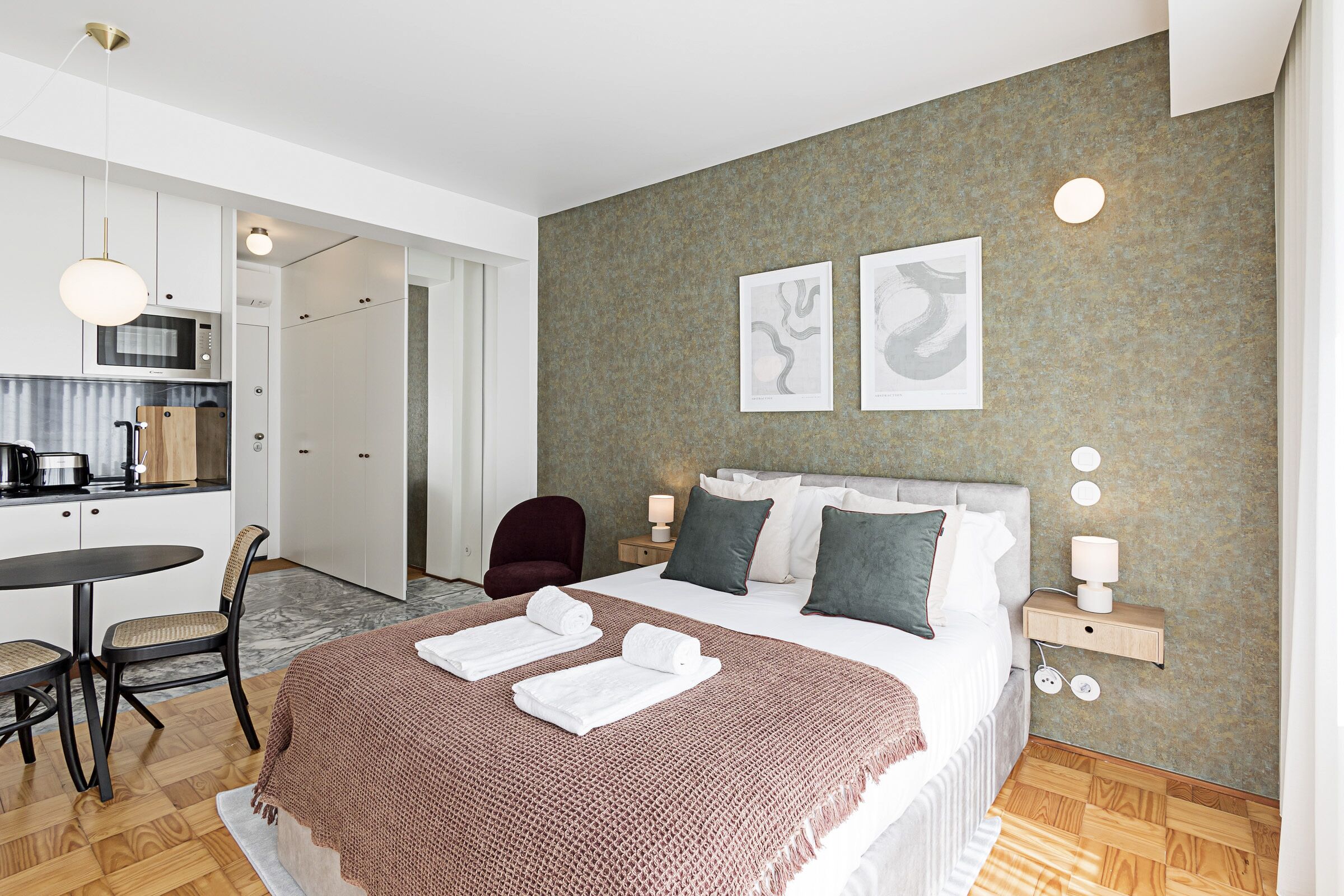 Ein modernes Hotelzimmer mit Bett, Nachttischen, einem Schreibtisch und einer Küchenzeile.