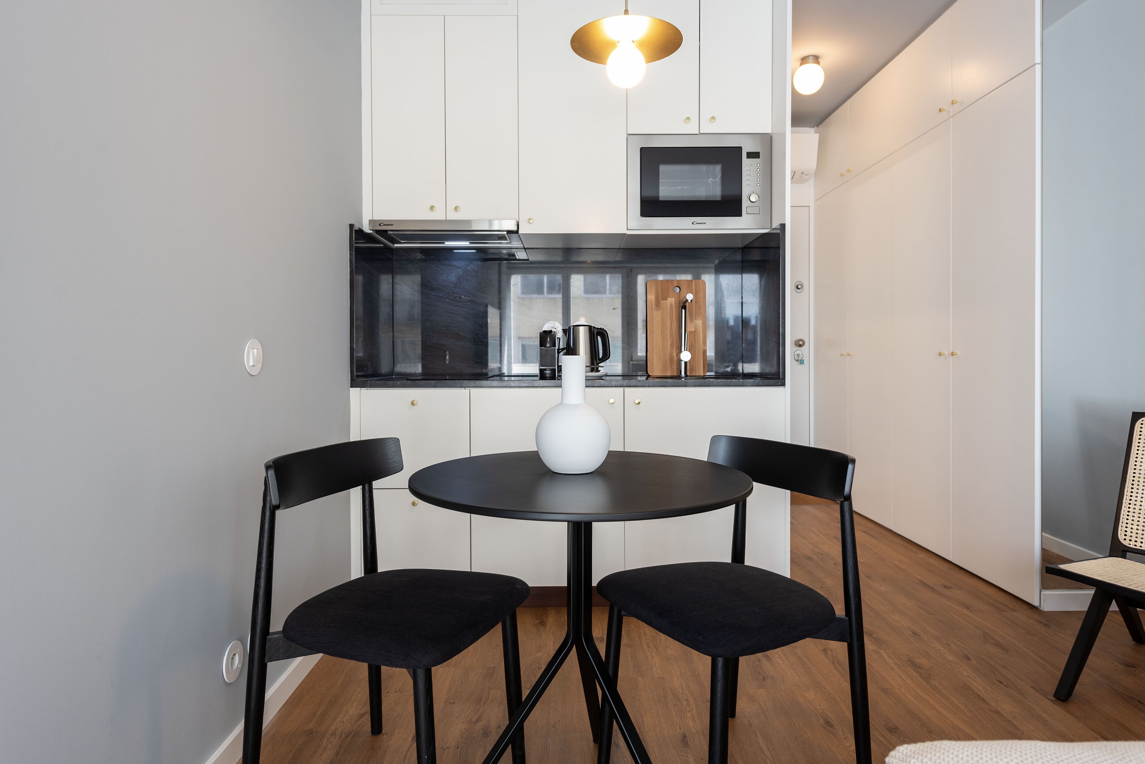 A modern kitchen with white cabinets, a black countertop, and a round table with two black chairs.