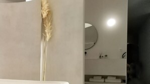Et moderne soveværelse med minimalistisk design, med en seng med hvide sengetøj, et stort spejl og dekorativ pampasgræs.