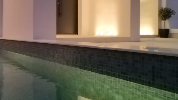 En moderne bygning med swimmingpool, karakteriseret ved buegange og en fliseterrasse.