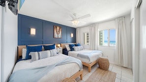 A bedroom with two beds, a ceiling fan, and a view of the beach.