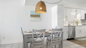 A modern kitchen with white cabinetry, a dining table with chairs, and a hanging pendant light.