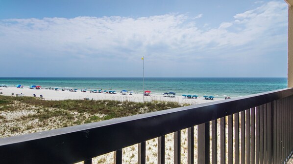 A beach with white sand and a clear sky. There are umbrellas and people on the beach.