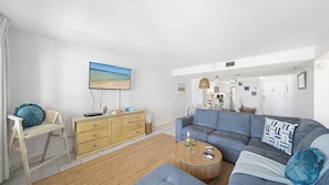 Ein Wohnzimmer mit einer Couch, einem Couchtisch, einem Fernseher und einem Essbereich im Hintergrund.
