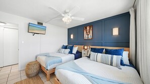 Ein Schlafzimmer mit zwei Betten, einem Deckenventilator, einem Fernseher und einem Bild an der Wand.