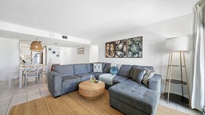 Una sala de estar moderna con un sofá seccional gris, una mesa de centro redonda y un comedor con una mesa y sillas blancas.