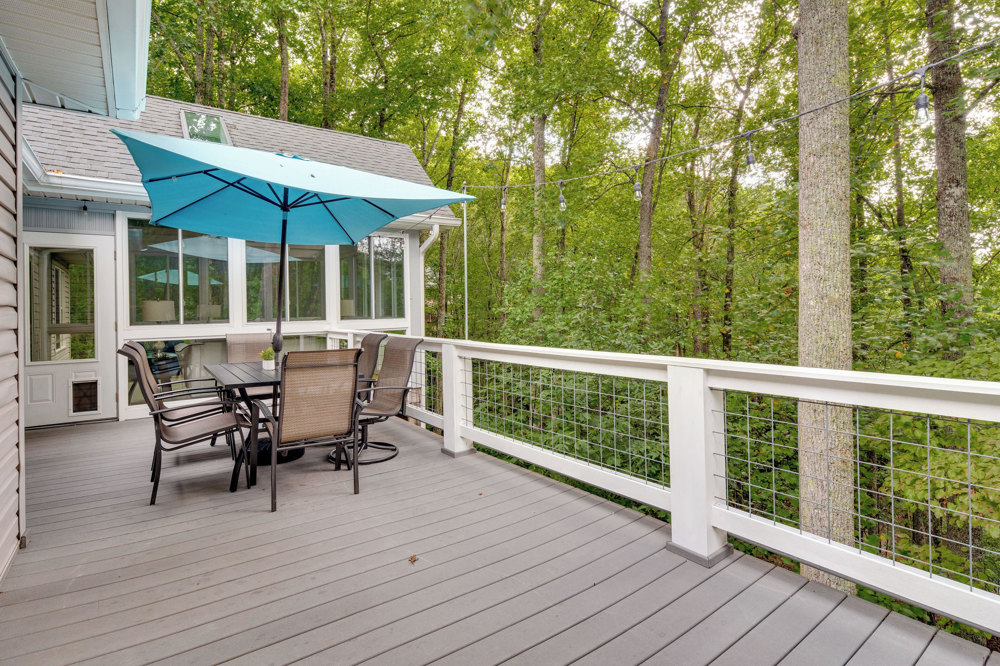 Une terrasse extérieure couverte, dotée d’une table et de chaises, entourée d’une balustrade blanche et offrant une vue sur une forêt.